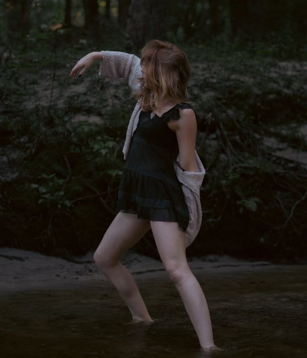 Woman in a calm, flowing movement pose against a dark background.